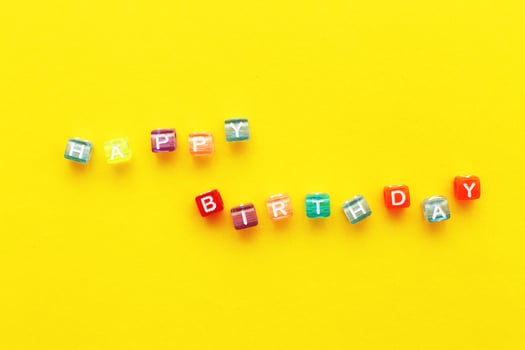 Happy birthday inscription made of colorful cubes beads on yellow background photo
