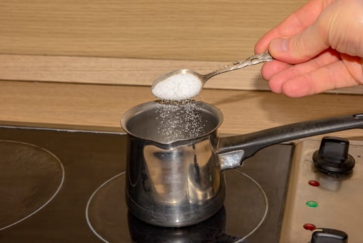 hand putting sugar with spoon in empty pot on stove photo