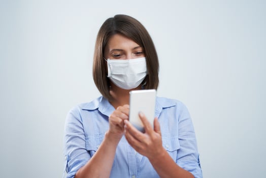 Attractive woman wearing protective mask holding smartphone isolated over white background photo