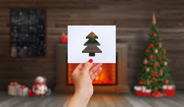 Hand holds a paper with a Christmas tree cut out on it. Fireplace with a fire, a Christmas tree and Christmas decorations photo