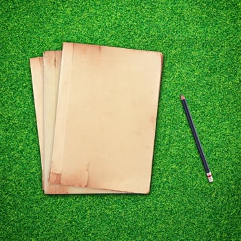 Pencil and old book on green grass background photo