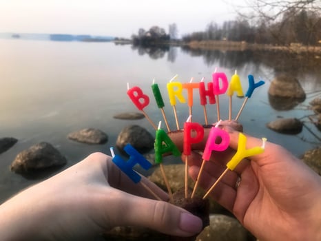 Happy birthday inscription made of holiday candles in the hands of a man and a woman opposite the water of the ocean lake river photo