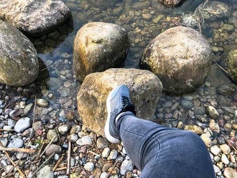 A foot in a sneaker steps on large round beautiful natural stones cobblestones in water, sea, lake, river. Concept tourism, outdoor activities photo