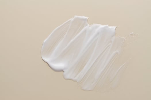 Texture of white cream on beige background. Smear of moisturizer close up. Lotion swatch. Beauty skin care product smear smudge. SPF sunscreen cream sample on beige background photo