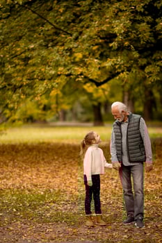 Grandfather spending time with his granddaughter in park on autumn day photo