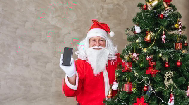 Santa claus celebrating Christmas in happiness and excitement while holding mobile phone beside the fully decorated christmas tree for sale promotion and online shopping usage photo