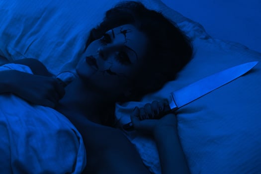 Spooky porcelain speaking doll holding knife and lying in the bed photo
