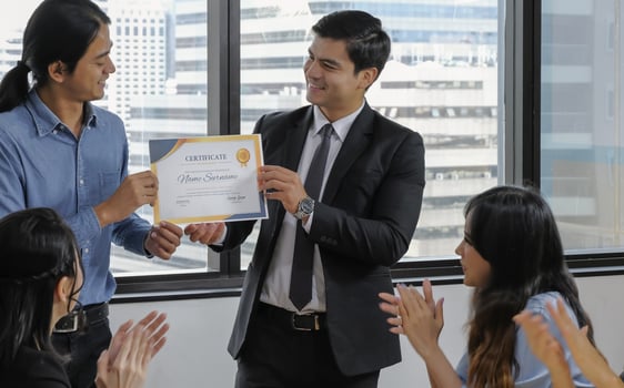 Young caucasian manager in suit giving mock up certificate to asian staff with happy smiling face while others applauding for congratulation in office meeting room. Selective focus. photo