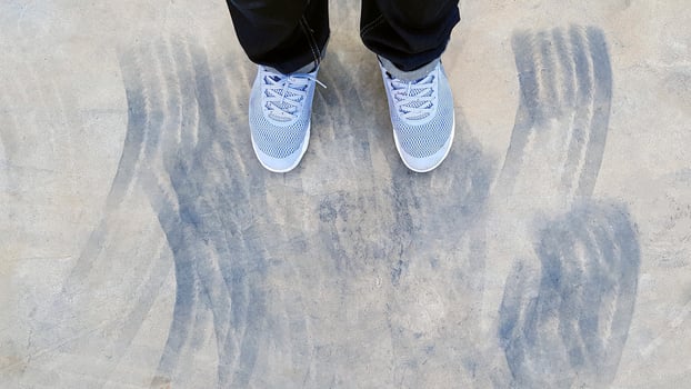 Top view of leg wearing blue jeans and gray or grey sneakers or fashion shoes on floor with car wheel or brake mark on road or street with copy space. Flat lay of part body. Abstract background photo