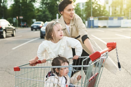 Happy mother and her daughters are having fun with a shopping cart on a parking lot beside a supermarket. photo