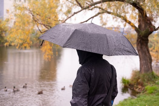 a man in a jacket with a hood, stands with his back with an umbrella in his hands, Against the background of the lake photo