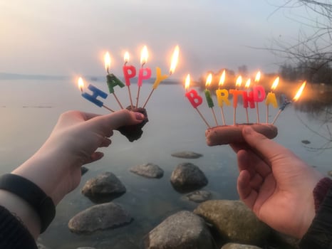Burning happy birthday inscription made of holiday candles in the hands of a man and a woman opposite the water of the ocean lake river. Concept birthday celebration in nature, outdoors photo