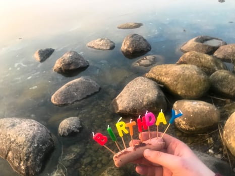 Happy birthday inscription made of holiday candles in the hands of a man and a woman opposite the water of the ocean lake river photo