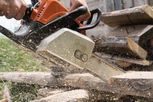 Male hands sawing old boards for firewood with a professional chainsaw, in a village yard. Winter preparation concept. Lifestyle. photo