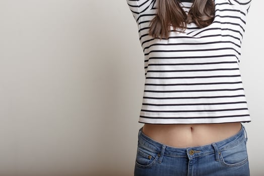 Confident girl in blue jeans and a striped sweater, raised her arms and extended her beautiful belly and slender waist. Copy space. photo
