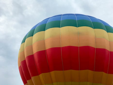 Large multi-colored bright round rainbow colored striped striped flying balloon with a basket against the sky in the evening photo