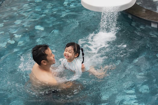 Asian father and daughter swimming playing slide pool in the pool at the resort, smiling and laughing. Having fun in the pool at the resort hotel, family happy concept. photo