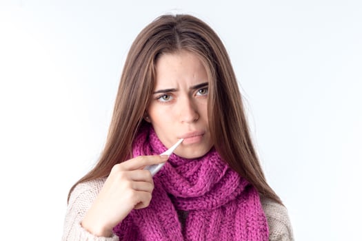 young girl in  warm scarf looks straight and keeps mouth thermometer is isolated on  white background photo