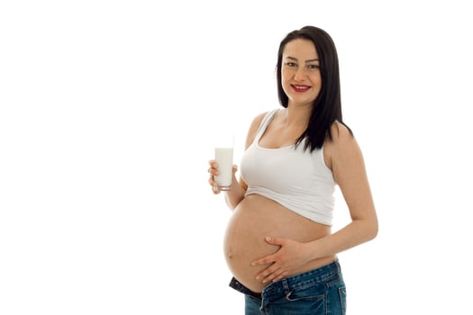 beautiful young pregnant brunette woman touching her belly and drinks milks isolated on white background photo