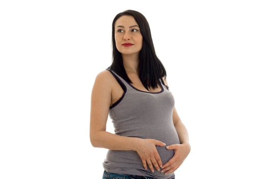 studio portrait of young pregnant brunette woman in shirt touching her belly and looking aside isolated on white background photo
