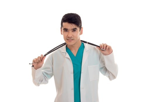 portrait of young beautiful brunette man doctor in white uniform with stethoscope looking at the camera isolated on empty background photo