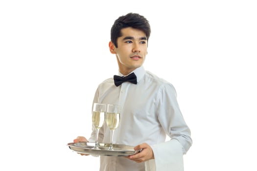 young handsome waiter holding a tray with glasses of champagne and looks toward photo