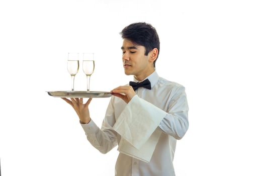 handsome young waiter with black hair stands straight looks away and holds a tray with two glasses photo