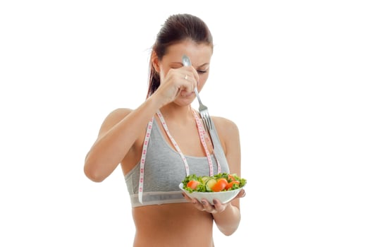 athletic girl in grey top holds a plate of salad with vegetables close-up photo