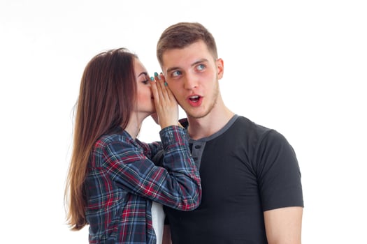 a young girl with long hair said something in guy ear covering the hands and he is surprised and opens his mouth photo