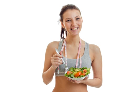 beautiful happy girl looking into the camera, laughing and holding a plate with vegetable salad closeup photo