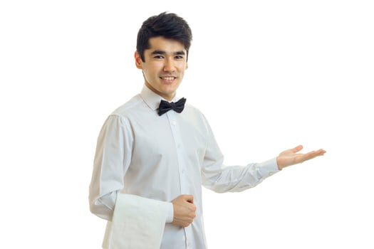 handsome waiter with black hair invites guests to the table with his hand and smiling photo
