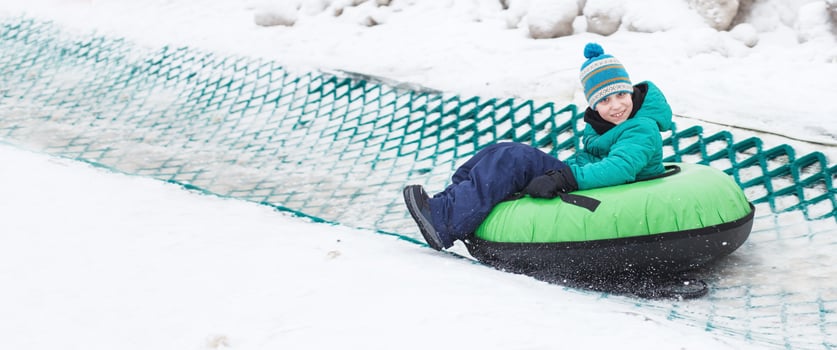 Child having fun on snow tube. Boy is riding a tubing. Winter entertainment. kid sliding downhill on tube. banner photo