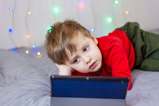 A cute boy is on the bed looking at a tablet. Online training, communication on the Internet. Funny smiling child. photo