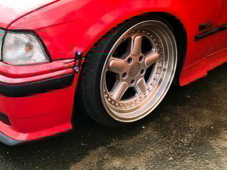Beautiful big racing wheels of a sports red car with a very low ground clearance on cast shiny expensive alloy wheels in the style of Stans. Tuning cars photo