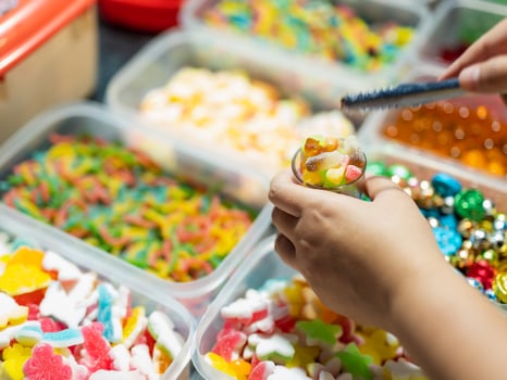 Sweets are sold in boxes and small baskets of jelly candies of various colors. Buyers are picking up glasses. photo