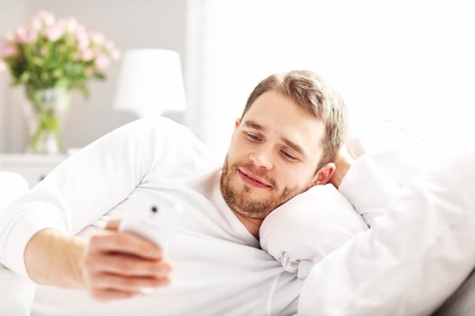 Handsome man lying in bed with smartphone photo