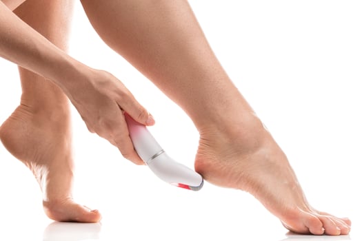 Female feet and electric foot file for callus and dead skin removal on white background photo