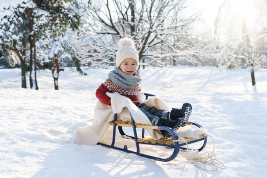 Toddler boy sitting on the sleigh in a snowy city park during sunny winter day photo