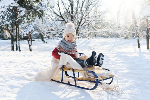 Toddler boy sitting on the sleigh in a snowy city park during sunny winter day photo