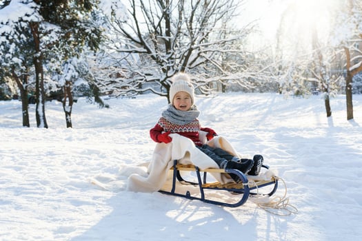 Toddler boy sitting on the sleigh in a snowy city park during sunny winter day photo