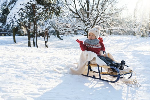 Toddler boy sitting on the sleigh in a snowy city park during sunny winter day photo