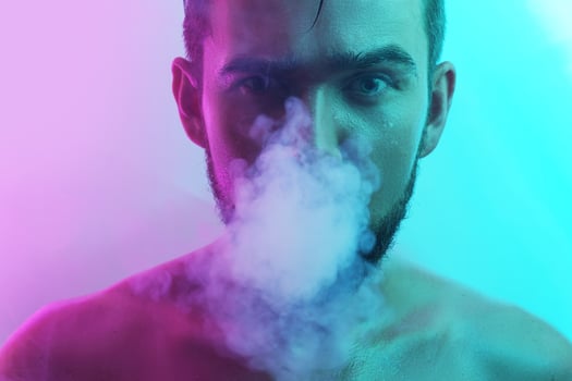 Handsome young man with wet skin in ultraviolet light smoking vape photo