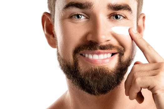 Young man is applying moisturizing and anti aging cream on his face photo
