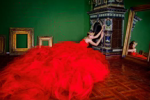 Beautiful woman in long red dress and in royal crown near fireplace in luxury interior in photo studio