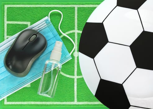Computer mouse, sanitizer, blue medical mask, empty plate like soccer ball placed on green felt mini football field, top view. Concept stay home during coronavirus and watch match broadcast online. photo