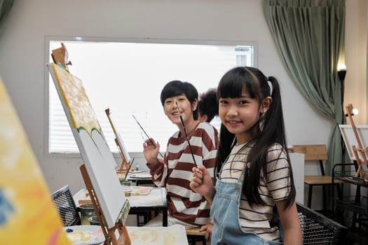 Portrait of Asian kids looking at camera and smiling with acrylic color picture painted on canvas in art classroom and creative learning with talents and skill at elementary school studio education. photo