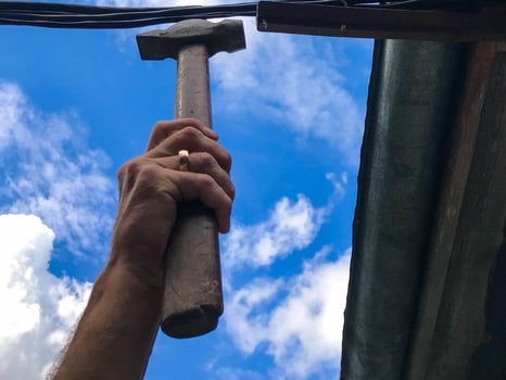 a man hammers nails with a hammer against the blue sky. repairs the roof of a wooden house. the man is wearing a gold ring. holds a hammer, carries out repair work at a height photo