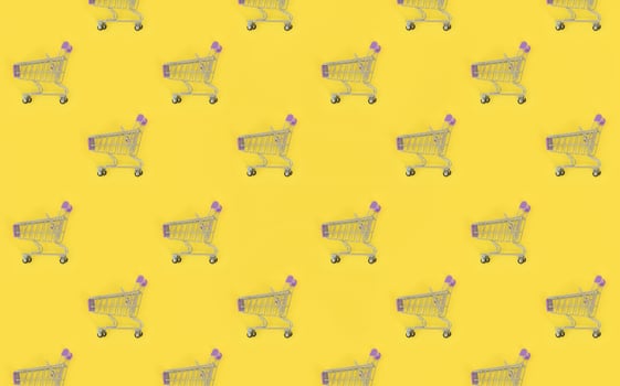 Shopping addiction, shopping lover or shopaholic concept. Many small empty shopping carts perform a pattern on a pastel colored paper background. Flat lay composition, top view photo