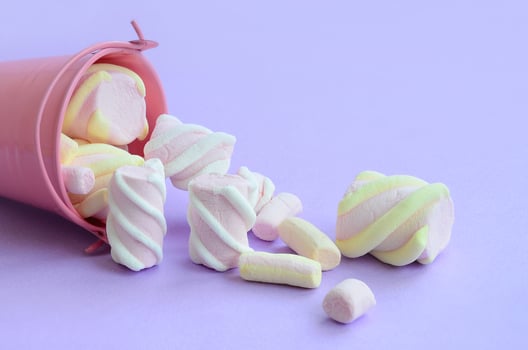 Overturned miniature pink bucket filled with marshmallow lies on a purple pastel background. Minimal concept photo