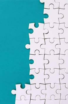 Fragment of a folded white jigsaw puzzle on the background of a blue plastic surface. Texture photo with copy space for text